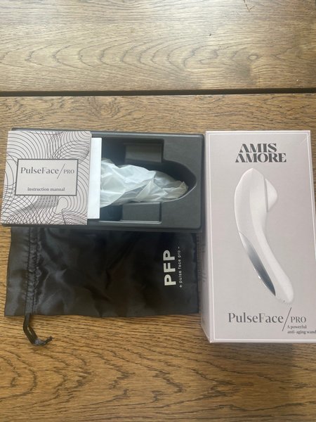 PulseFace PRO microcurrent device i originalförpackning som är öppnad – vit ansiktsapparat på träbord